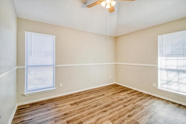 unfurnished room featuring lofted ceiling, ceiling fan, a textured ceiling, and wood finished floors