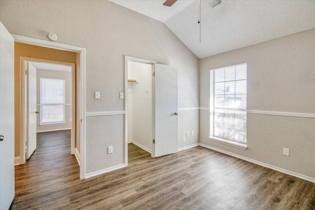 unfurnished bedroom with baseboards, lofted ceiling, wood finished floors, a walk in closet, and a closet