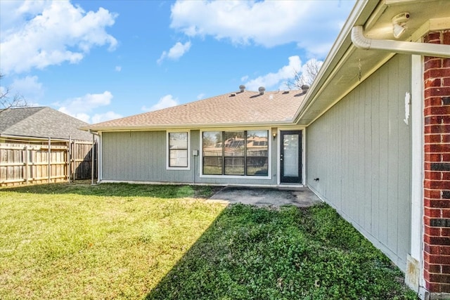 back of property with a shingled roof, brick siding, a lawn, and fence