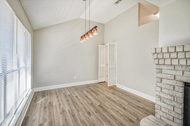 unfurnished dining area with visible vents, baseboards, lofted ceiling, wood finished floors, and a brick fireplace