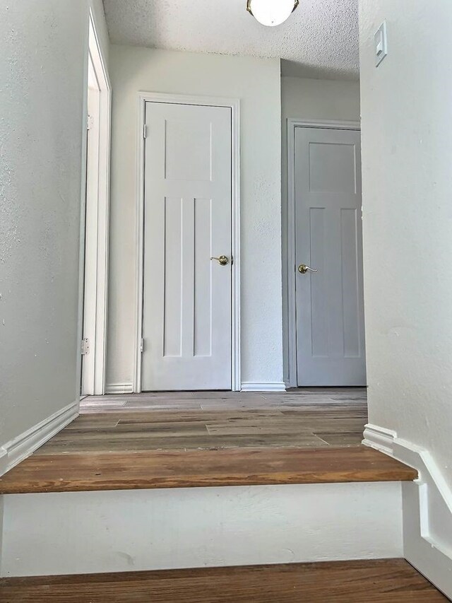interior space featuring a textured ceiling, wood finished floors, and baseboards