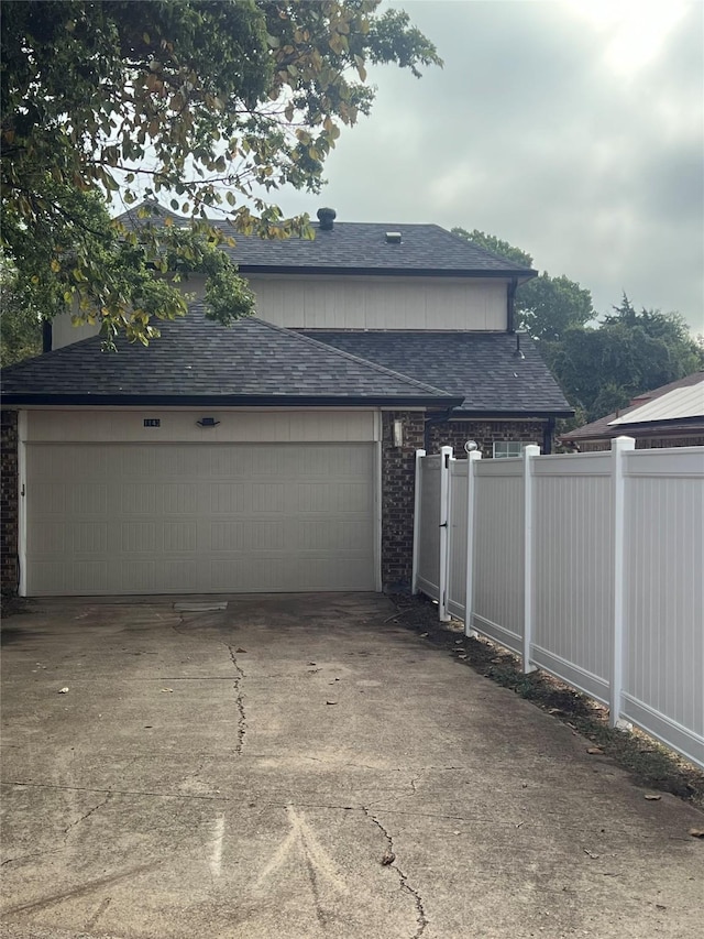 view of home's exterior featuring a garage, concrete driveway, a shingled roof, and fence