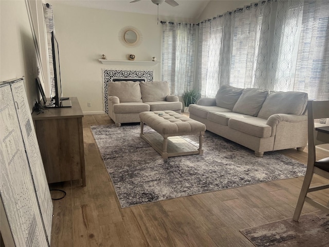 living area featuring ceiling fan, vaulted ceiling, a tile fireplace, and wood finished floors