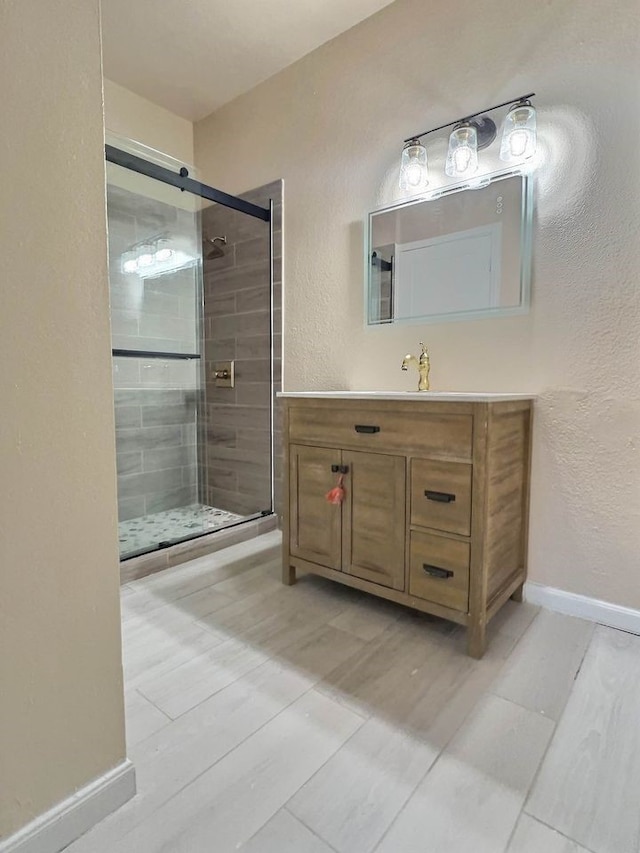 bathroom with a textured wall, a shower stall, baseboards, and vanity