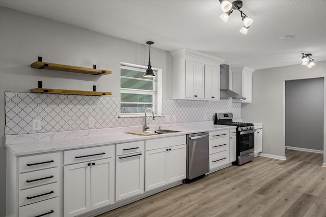 kitchen with light wood finished floors, stainless steel appliances, white cabinetry, a sink, and wall chimney exhaust hood