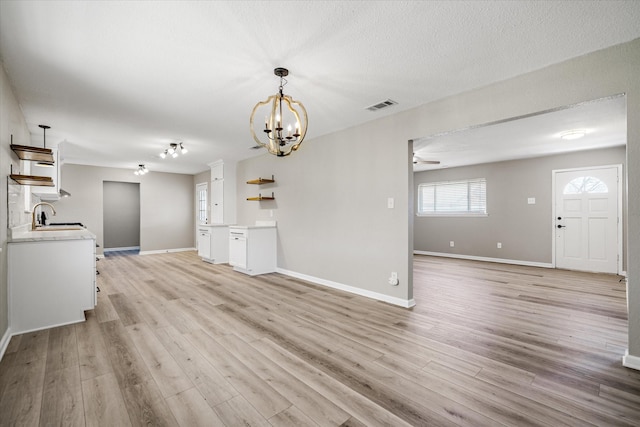 unfurnished living room with light wood-style floors, visible vents, a sink, and baseboards