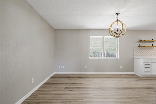 unfurnished dining area featuring baseboards, a notable chandelier, and light wood finished floors