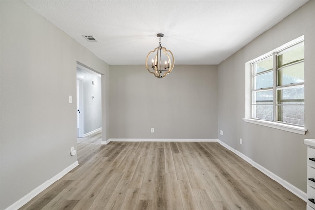 spare room featuring light wood finished floors, an inviting chandelier, visible vents, and baseboards