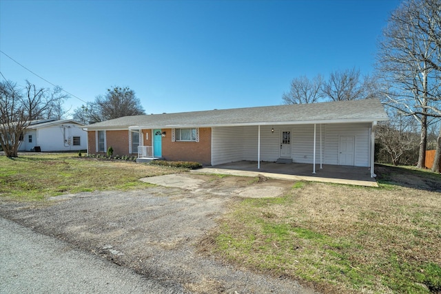 single story home with a front yard, brick siding, an attached carport, and dirt driveway