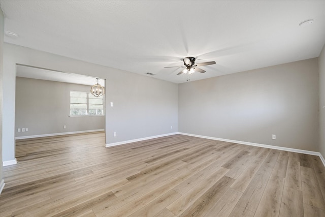 spare room featuring ceiling fan with notable chandelier, light wood finished floors, visible vents, and baseboards