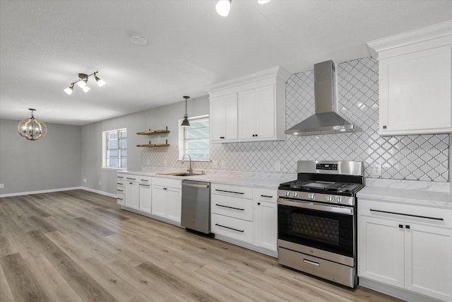 kitchen featuring light wood-style flooring, a sink, wall chimney range hood, appliances with stainless steel finishes, and backsplash