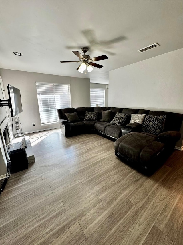 living room with ceiling fan, a glass covered fireplace, wood finished floors, and visible vents