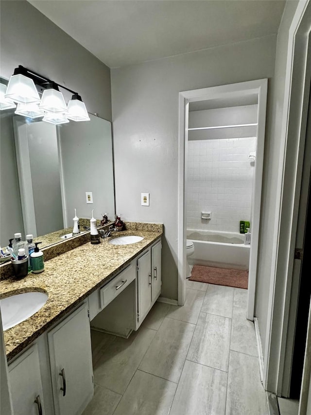 bathroom with double vanity, a sink, toilet, and baseboards