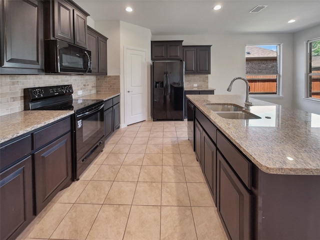 kitchen with light tile patterned floors, a sink, visible vents, black appliances, and an island with sink