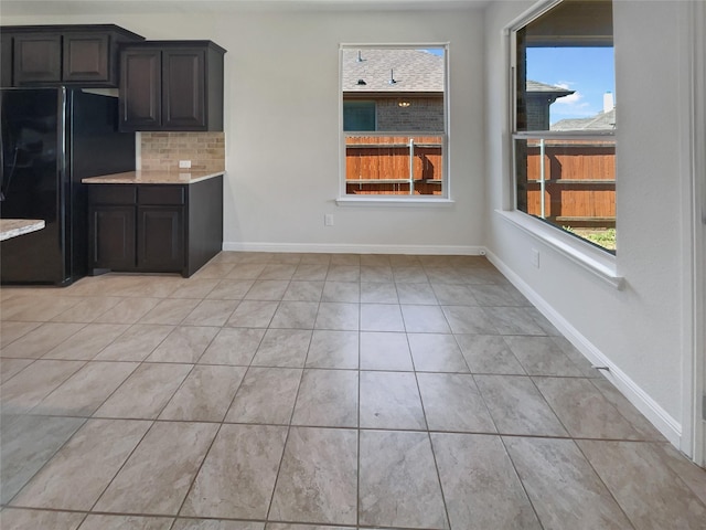 kitchen with light tile patterned flooring, baseboards, light countertops, freestanding refrigerator, and decorative backsplash