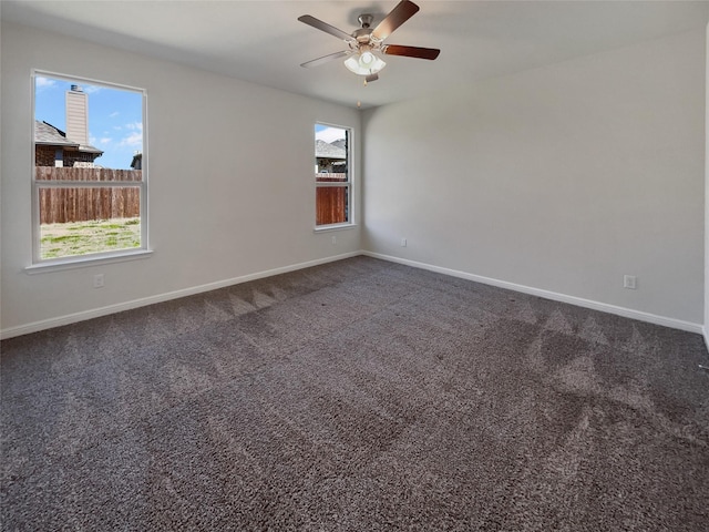 empty room with baseboards, dark carpet, and ceiling fan