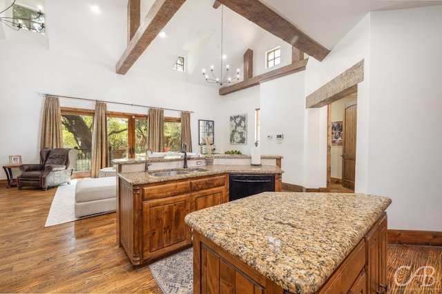 kitchen with black dishwasher, a center island with sink, open floor plan, a sink, and beam ceiling