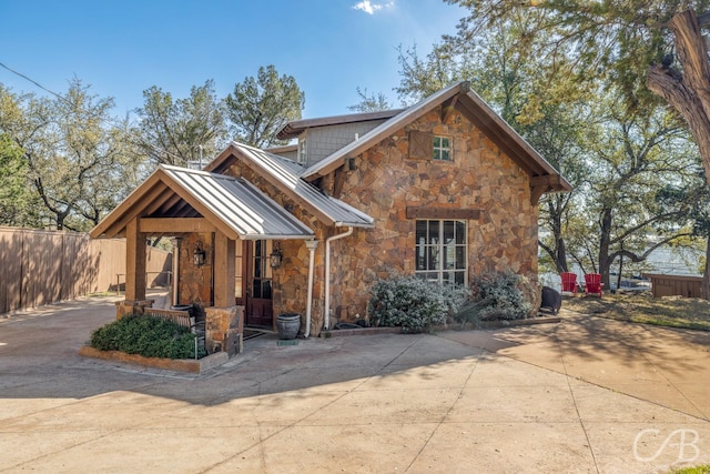 view of front of house with stone siding, a standing seam roof, fence, and metal roof