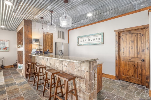 bar featuring visible vents, baseboards, stainless steel refrigerator with ice dispenser, indoor wet bar, and stone tile flooring