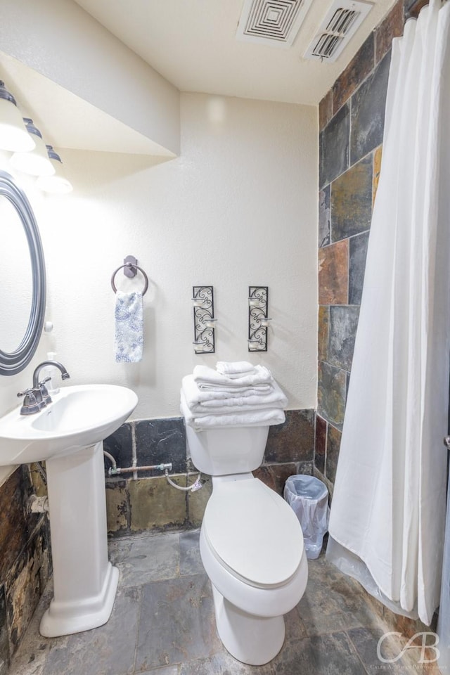 full bathroom with toilet, a shower with curtain, stone tile floors, and visible vents