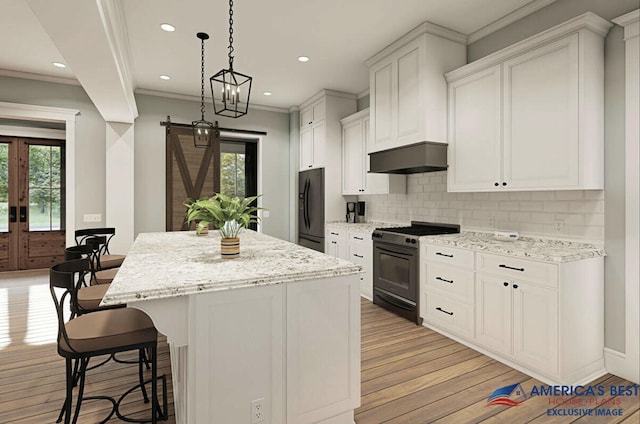 kitchen with a barn door, a kitchen island, exhaust hood, freestanding refrigerator, and range with gas cooktop