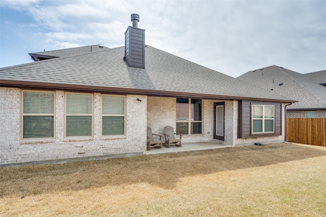 back of house with a patio, fence, a shingled roof, brick siding, and a chimney