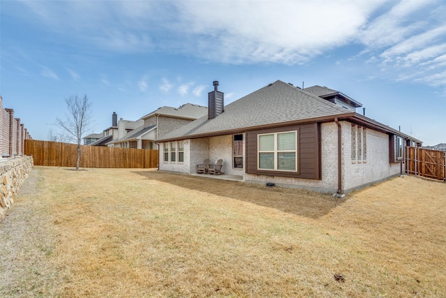 back of property featuring brick siding, a shingled roof, a lawn, a chimney, and a fenced backyard