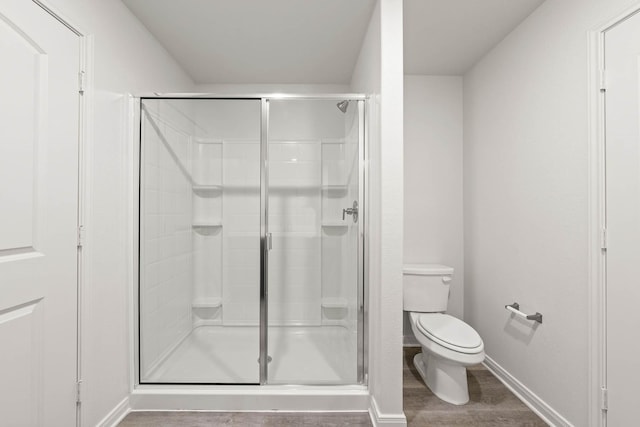 bathroom with a stall shower, wood finished floors, toilet, and baseboards