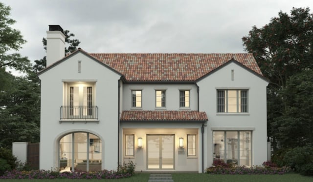 back of house featuring a tile roof, a yard, a chimney, stucco siding, and a balcony