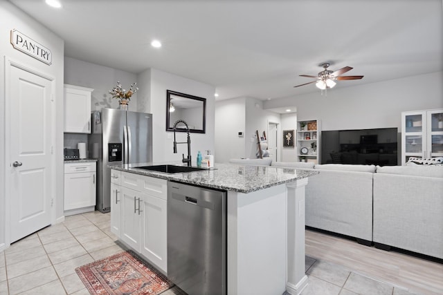 kitchen with a center island with sink, white cabinets, appliances with stainless steel finishes, light stone countertops, and a sink