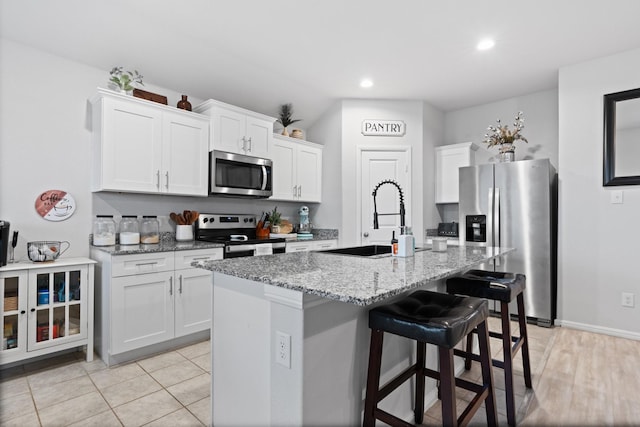 kitchen featuring light stone counters, appliances with stainless steel finishes, white cabinetry, a sink, and a kitchen bar