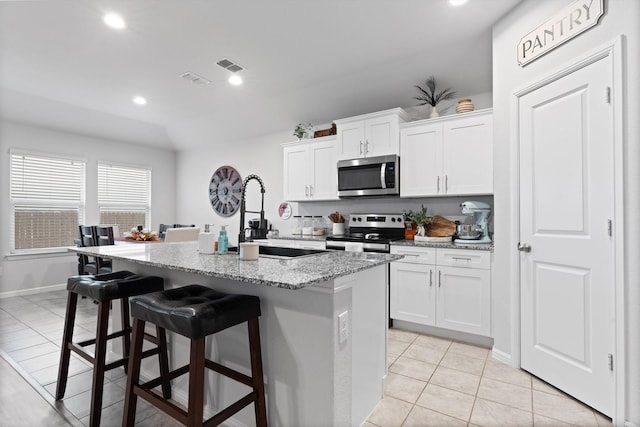 kitchen featuring light tile patterned floors, visible vents, a kitchen breakfast bar, light stone countertops, and stainless steel appliances