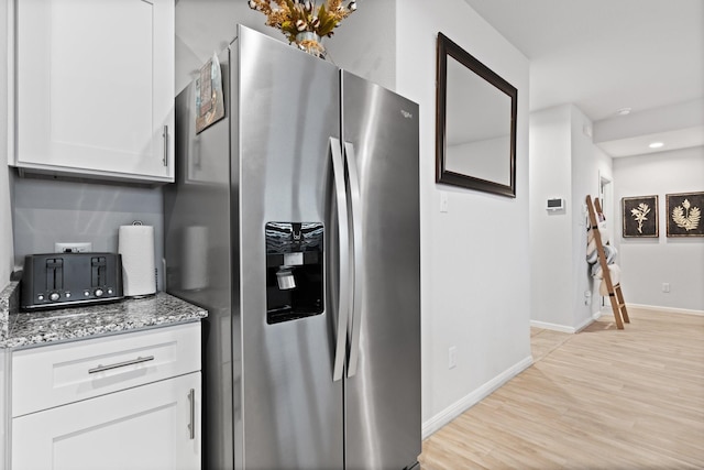 kitchen with white cabinets, stainless steel fridge, light wood finished floors, and light stone countertops