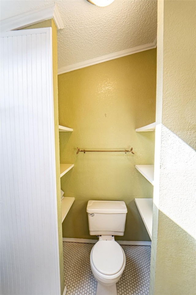 bathroom featuring a textured wall, toilet, ornamental molding, tile patterned floors, and a textured ceiling