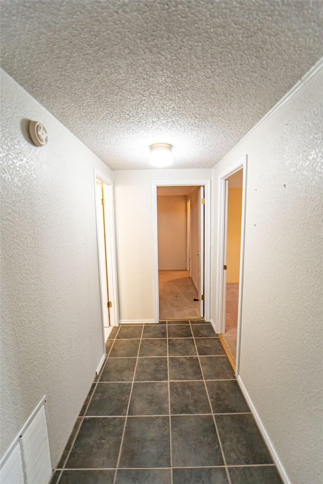 corridor with visible vents, a textured wall, dark tile patterned floors, and a textured ceiling