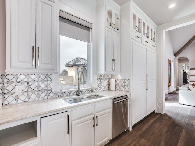 kitchen with light stone counters, arched walkways, stainless steel dishwasher, white cabinets, and a sink