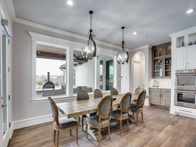 dining room featuring light wood-type flooring, arched walkways, crown molding, and recessed lighting