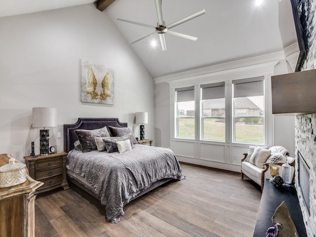 bedroom with ceiling fan, wood finished floors, beamed ceiling, a stone fireplace, and high vaulted ceiling