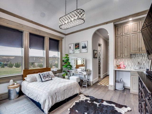 bedroom featuring arched walkways, baseboards, light wood-style flooring, ornamental molding, and a sink