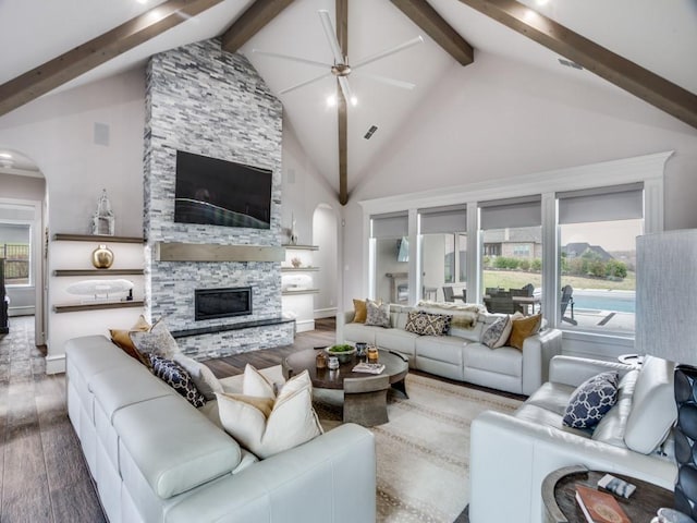 living room with arched walkways, a stone fireplace, beamed ceiling, and wood finished floors