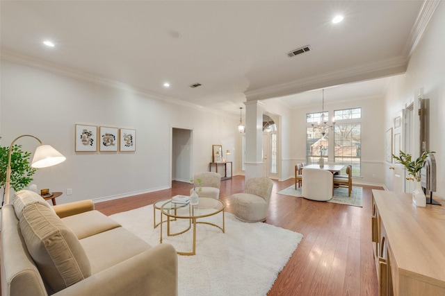 living area featuring baseboards, visible vents, an inviting chandelier, crown molding, and light wood-type flooring