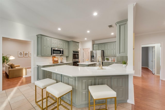 kitchen featuring a breakfast bar area, green cabinets, stainless steel appliances, and light countertops