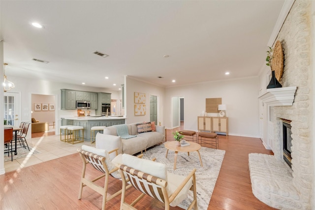 living area featuring crown molding, light wood-style floors, visible vents, and a fireplace