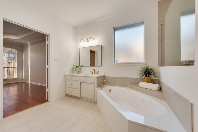 bathroom with wood finished floors, a tub with jets, vanity, and a wealth of natural light