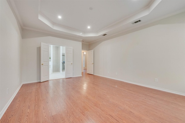 unfurnished room with light wood-style floors, a raised ceiling, crown molding, and baseboards