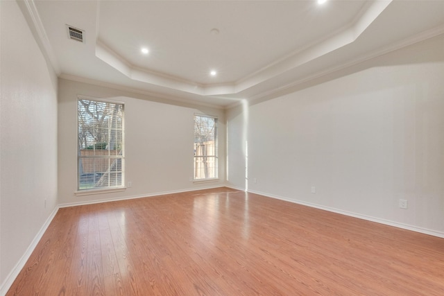 unfurnished room with light wood-style flooring, visible vents, baseboards, ornamental molding, and a tray ceiling