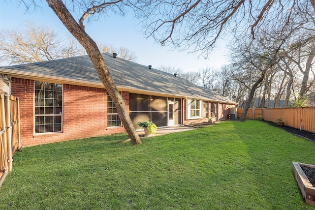 rear view of property featuring a yard, brick siding, a shingled roof, and a fenced backyard