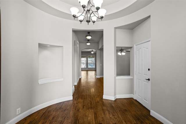 hallway featuring a tray ceiling, arched walkways, a notable chandelier, wood finished floors, and baseboards