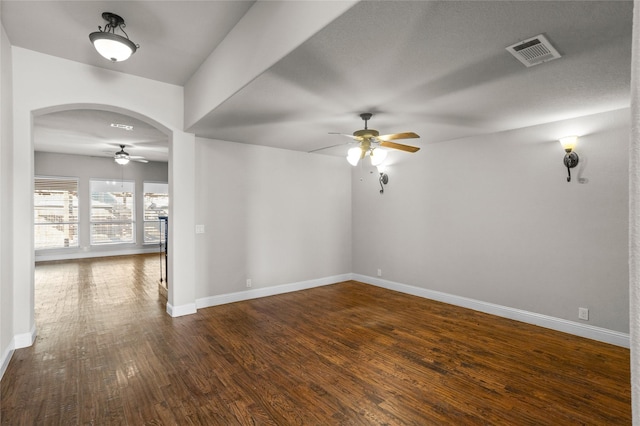 spare room featuring arched walkways, visible vents, baseboards, a ceiling fan, and dark wood finished floors