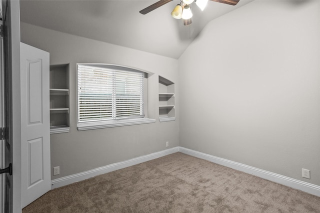 unfurnished room featuring built in shelves, a ceiling fan, baseboards, vaulted ceiling, and carpet